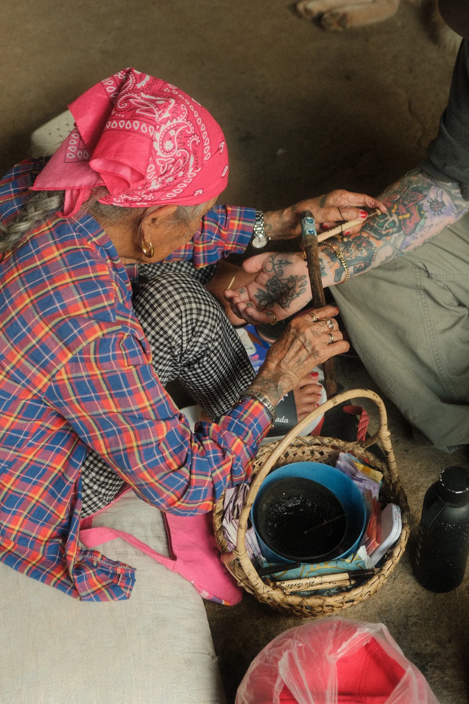 Apo Whang-Od at work, hands covered in her own ink, tapping a thorn into Steve's leg with a bamboo stick.