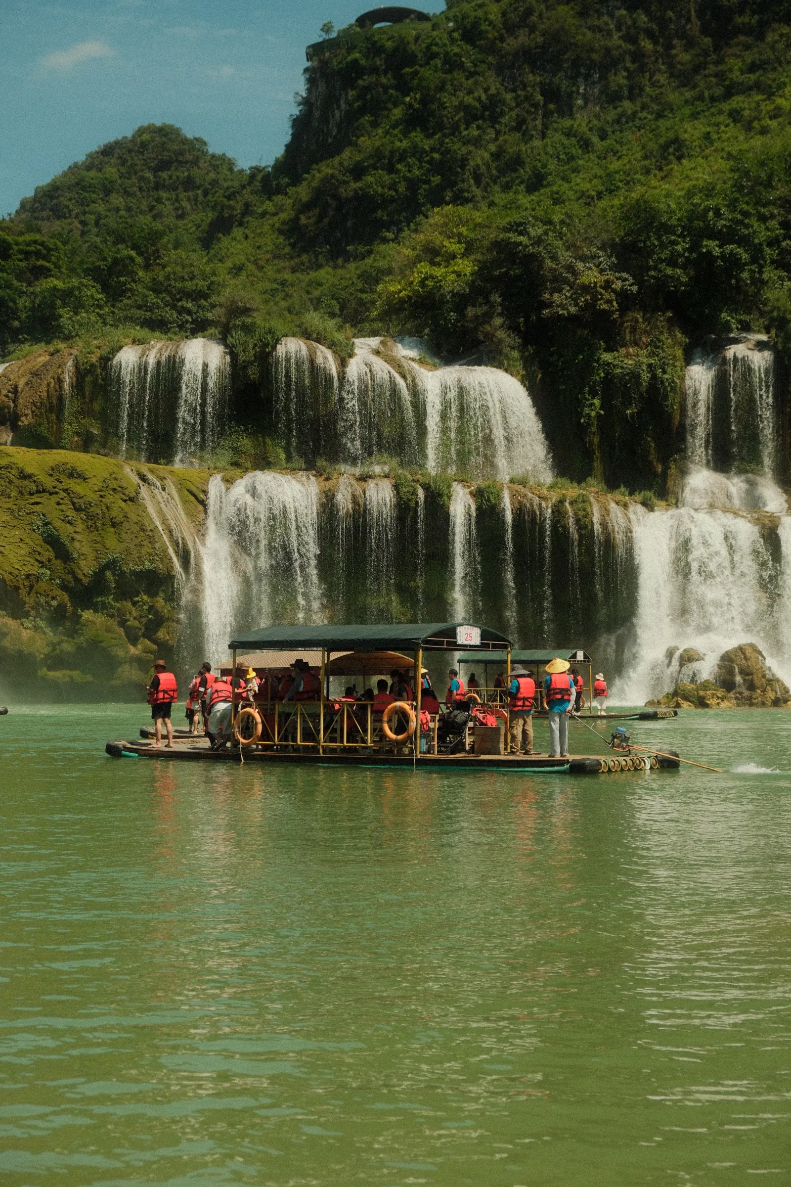 Ban Gioc waterfall: a wide tiered cascade with a tour boat in the foreground.