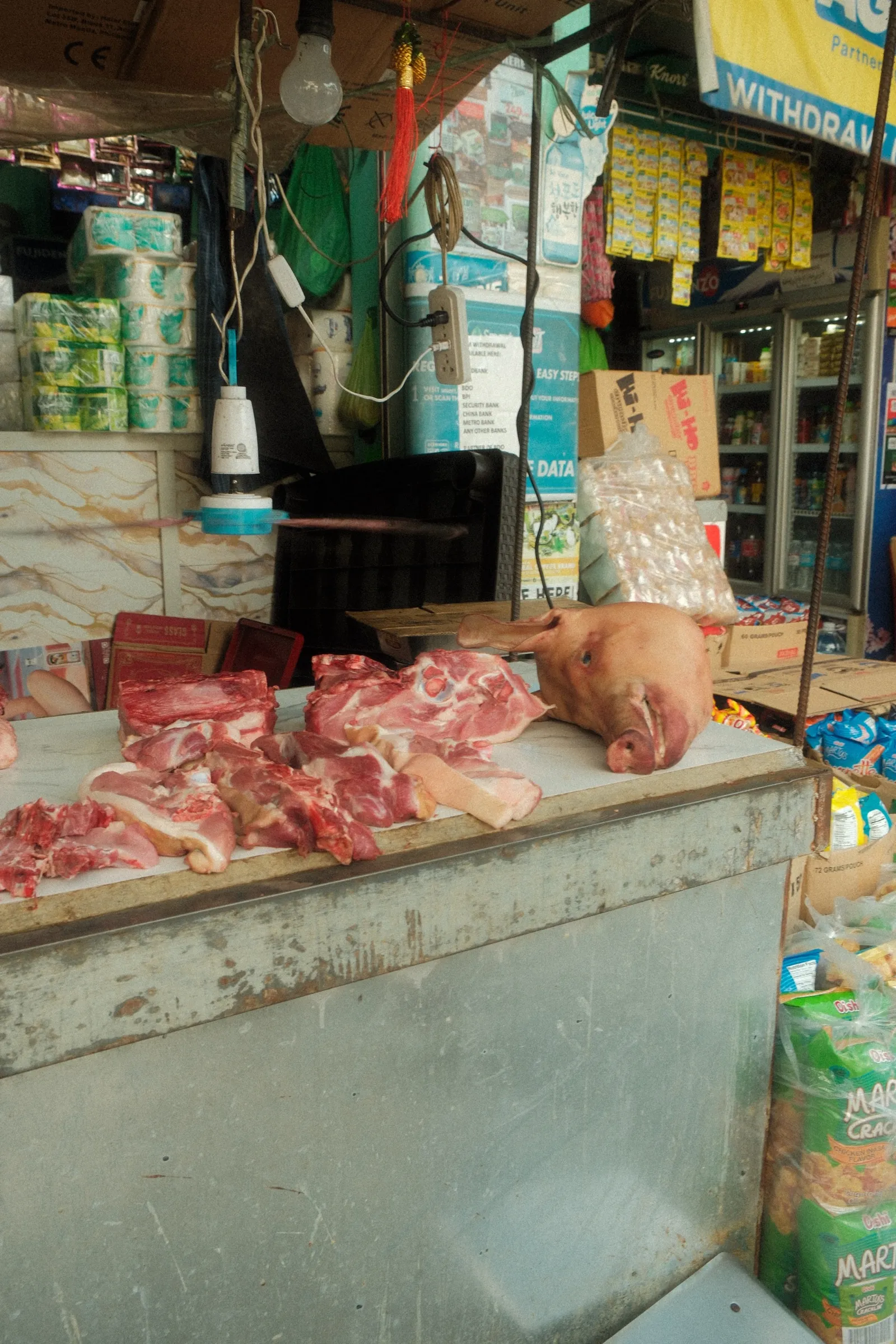 A butcher stand in Bontoc with a pig head sitting on the counter beside cuts of fresh meat.