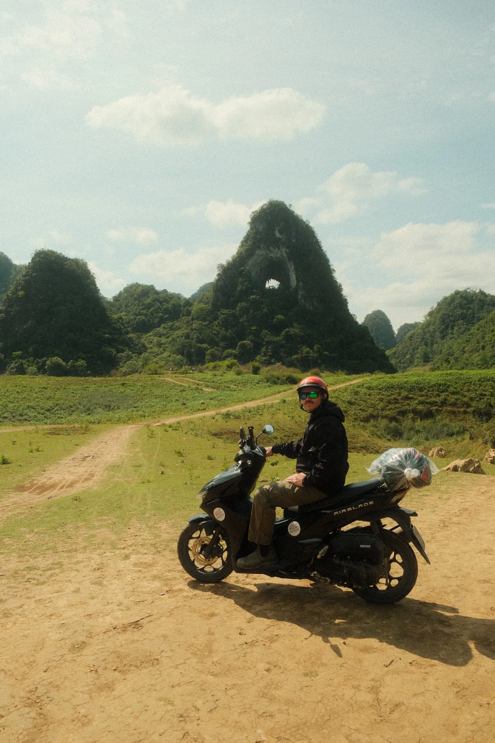 Me sitting on the scooter in front of God's Eye, the hole through the karst visible behind me.