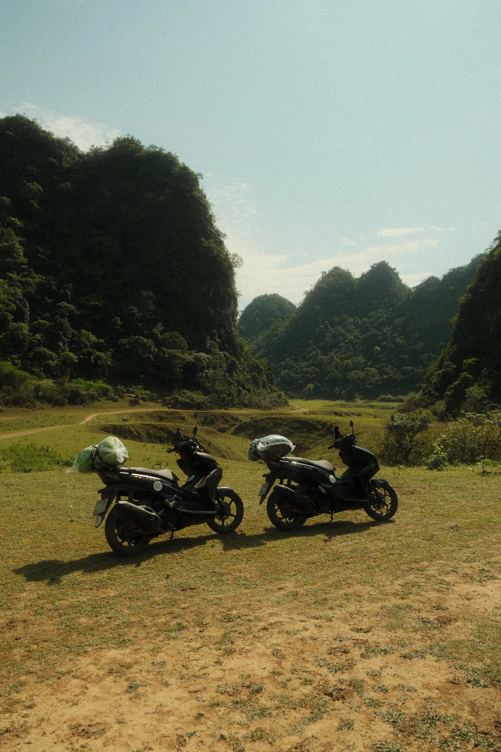 Two scooters parked in a field with karst mountains rising in the background.